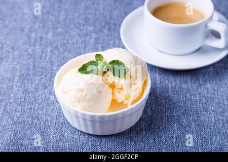 Vanilleeis mit Minze auf einem weißen Teller und einer Tasse Espresso auf blauem Hintergrund. Hausgemachtes Eis. Nahaufnahme. Stockfoto