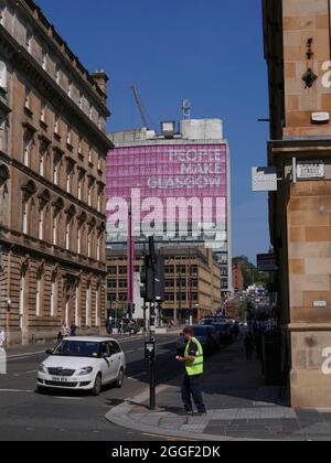 Ein Mann in einer Jacke wartet darauf, die Straße vor dem „People Make Glasgow“ am ehemaligen City of Glasgow College zu überqueren. North Hanover Street Glasgow, Schottland Stockfoto