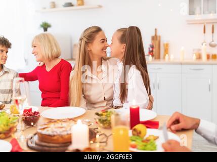 Nettes Mädchen berührt Nasen mit Mama an festlichen Tisch, feiern Familienurlaub zusammen mit ihren Nasen, leckeres Essen zusammen, genießen bondi Stockfoto