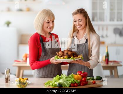 Porträt einer jungen Frau mit ihrer älteren Mutter, die Gericht mit traditionellem truthahn hält, Weihnachten oder Thanksgiving-Dinner kocht und festliche Familien zubereitet Stockfoto