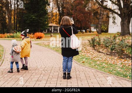 Moskau, Russland, Oktober 2019 - eine Reisende Mutter fotografiert auf ihrem Smartphone die Landschaft im Herbstpark. Ihre Kinder gehen in der Nähe Stockfoto