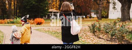 Moskau, Russland, Oktober 2019 - eine Reisende Mutter fotografiert auf ihrem Smartphone die Landschaft im Herbstpark. Ihre Kinder gehen in der Nähe Stockfoto