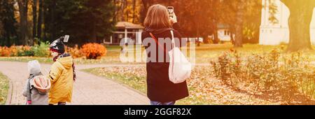Moskau, Russland, Oktober 2019 - eine Reisende Mutter fotografiert auf ihrem Smartphone die Landschaft im Herbstpark. Ihre Kinder gehen in der Nähe Stockfoto