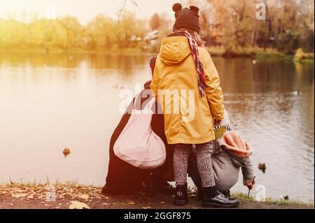 Mutter und ihr Mädchen füttern Enten in einem Teich und bewundern die Herbstlandschaft bei einem Spaziergang im Herbstpark. Das Konzept einer Familie lokalen t Stockfoto