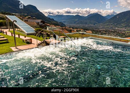 Wasser fließt über die Stufen eines Infinity-Pools im Wellnessbereich auf dem Dach des Hotels Hohenwart in Schenna, Südtirol, Italien, mit einem weitläufigen Blick über das Etschtal. Die Vier-Sterne-Superior-Unterkunft verfügt über einen Spa- und Wellnessbereich mit einem Panoramapool. Stockfoto