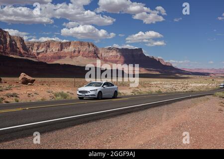 Ein Auto rast entlang der Route 89A und verschwindet in der Ferne am Fuße des Vermilion Cliffs National Monument, das entlang des Colorado River nea verläuft Stockfoto