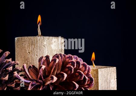 Zwei goldene Kerzen brennen mit Tannenzapfen auf schwarzem Hintergrund. Stockfoto