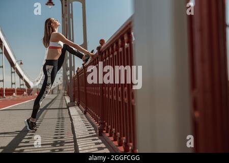 Eine ruhige, schlanke Frau streckt die Beine am Handlauf auf einem schmalen Steg Stockfoto