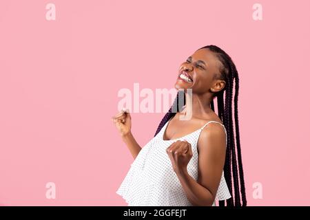Emotionale schwarze Dame mit Afro-Bündchen, die YES-Geste machen, sich auf rosafarbenem Studiohintergrund triumend fühlen, Raum kopieren. Überglücklich afroamerikanische Frau Stockfoto