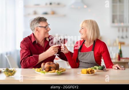 Liebevolles Seniorenpaar, das romantische Zeiten hat, Rotwein trinkt, während es festliches Thanksgiving oder Weihnachtsessen in der Küche kocht. Älterer Mann und sein W Stockfoto