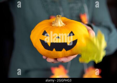 Orange Kürbis Kopf für Halloween in der Hand. Scary Kopf Jack o Laterne mit Herbstblättern fallen. Gruselig Lächeln Horror Stockfoto