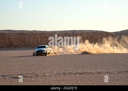 Ein schwarzes Auto oder ein Pickup-Truck treibt einen Sand und spritzt Sand in der Luft und in der Dasht e lut- oder sahara-Wüste herum. Stockfoto