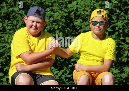 Zwei Jungen in gelben T-Shirts schütteln sich im Sommer im Park die Hände. Hochwertige Fotos Stockfoto