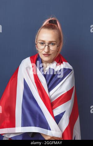 Junge Frau Expat in Brillen mit Großbritannien Flagge. Studioaufnahme. Hipster-Lehrerin in englischer Sprache. Fashionly gekleidete Frau mit rosa Haaren in bla Stockfoto