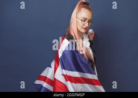 Junge Frau Expat in Brillen mit Großbritannien Flagge. Studioaufnahme. Hipster-Lehrerin in englischer Sprache. Fashionly gekleidete Frau mit rosa Haaren in bla Stockfoto