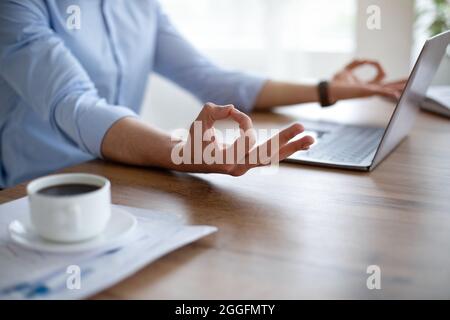 Nicht erkennbarer arabischer Typ, der vor dem Laptop-pc meditiert, mit beiden Händen Gyan-Mudra macht, am Arbeitsplatz Ruhe zu bewahren versucht, Nahaufnahme. Stressmanagement Stockfoto