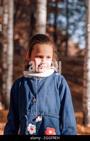 Close up glücklich Kind Konzept. Nettes kleines Mädchen in blauen Jeans Mantel mit Stickerei Blumen im Herbst Wald Hintergrund Stockfoto