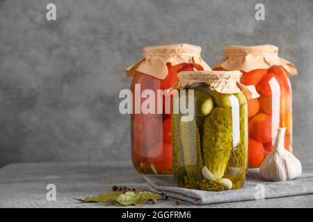 Hausgemachte eingelegte Tomaten und Gurken. Gemüsekonserven in Gläsern auf grauem Tisch. Speicherplatz kopieren. Herbsternte und Vorbereitungen. Stockfoto