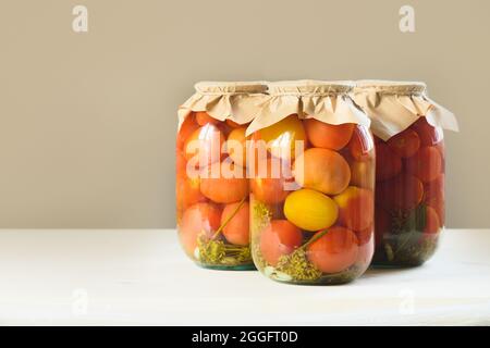 Hausgemachte saure marinierte Tomaten in Gläsern auf beigem Hintergrund. Gemüsekonserven. Stockfoto