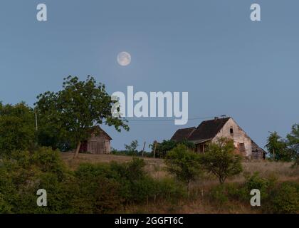 Verlassene Bauernhaus und Schuppen in der Landschaft und Vollmond aufgehen Stockfoto