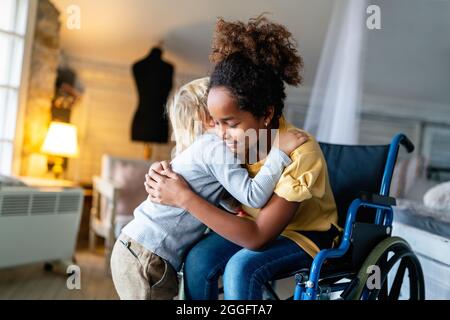 Schwarzes kleines Mädchen mit Behinderung im Rollstuhl, das sich mit ihrem jüngeren Bruder umarmt. Stockfoto