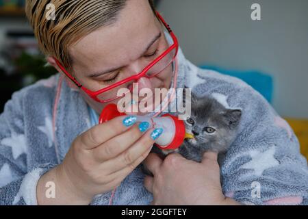 Porträt einer Frau mittleren Alters, die ein niedliches Kätzchen mit einer Milchflasche füttert Stockfoto