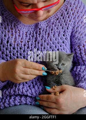 Porträt einer reifen Frau, die ein niedliches Kätzchen füttert pâté mit einem Löffel Stockfoto