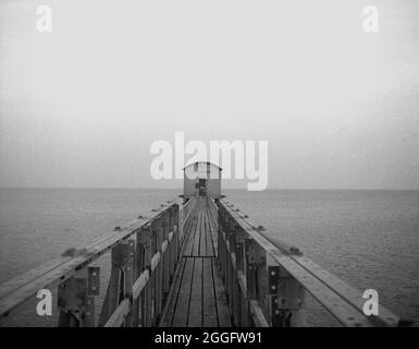 1950, historisch, Blick entlang der hölzernen Gangway zur alten Rettungsbootstation in Selsey, West Sussex, England, Großbritannien. 1861 wurde in Selsey ein Rettungsboot-Service eingerichtet. Im Jahr 1927 wurde das Bootshaus neu gebaut, um das neue Motorlifeboat der Station zu beherbergen, und diese Struktur ist hier zu sehen. Diese Gleisstation wurde in den späten 1950er Jahren wieder aufgebaut, wurde aber 2017 abgesetzt. Stockfoto