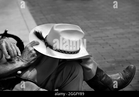 In Santa Fe, New Mexico, sitzt ein Mann in westlicher Kleidung auf einer Parkbank mit seinem Hut auf dem Knie. Stockfoto