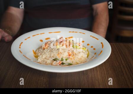 Risotto mit Krebsen und Spargel in Weißweinsauce mit Lachstartare gekrönt. Serviert in einem weißen Gericht auf einem dunklen Holztisch. Der Körper und von einem m Stockfoto