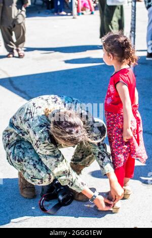 Rota, Spanien. August 2021. Ein Seemann der US-Marine repariert den gebrochenen Schuh eines jungen afghanischen Evakuierten, nachdem er am 30. August 2021 in Rota, Spanien, einen Flug aus Kabul bei der Ankunft in der Naval Air Station Rota verlassen hatte. NAS Rota stellt im Rahmen der Operation Allies Refuge eine temporäre Unterkunft für Evakuierte aus Afghanistan bereit.Quelle: MC1 Nathan Zimmerer/USA Navy/Alamy Live News Stockfoto