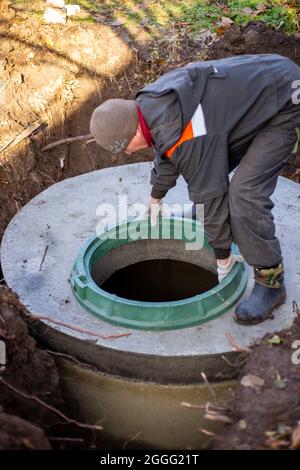 Ein Arbeiter installiert einen Kanalschacht an einem Klärbecken aus Betonringen. Bau von Abwasserentsorgungsanlagen für Privathäuser. Stockfoto