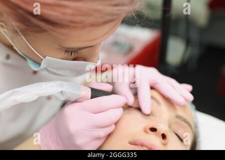 Meister in schützende medizinische Maske machen dauerhafte Augen Make-up für Kunden im Schönheitssalon Stockfoto