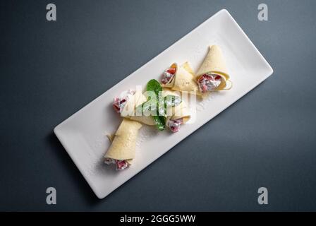Draufsicht auf dünne Pfannkuchenbrötchen mit Quark und Erdbeere auf weißem Teller Stockfoto