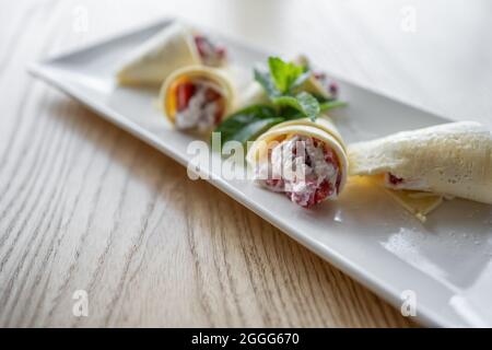 Dünne Pfannkuchenrollen mit Quark und Erdbeere auf Holzhintergrund Stockfoto