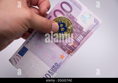 Männliche Hand mit goldenem Bitcoin und einer Euro-Banknote. Goldene BTC-Münze aus Kryptowährung und eine fünfhundert-Euro-Banknote, die an den Fingern eines Mannes gehalten wird Stockfoto