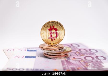 Goldene Bitcoin-Münze mit Logo-Symbol in roter Farbe auf 500-Euro-Banknoten eingegeben. Silberbitcoin liegt auf fünfhundert Euro-Banknoten. Stockfoto