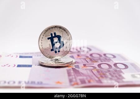 Silberne Bitcoin-Münze mit Logo-Symbol in blauer Farbe auf 500-Euro-Banknoten eingegeben. Silberbitmünze auf fünfhundert Euro-Banknoten. Stockfoto