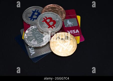 Verschiedene glänzende Bitcoin-Münzen, mit VISA-Debit- und Kreditkarten auf einem dunklen Hintergrund. BTC elektronische virtuelle Geldwährung. Stockfoto