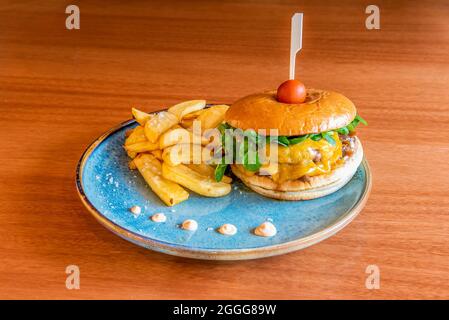 Burger mit zwei Fleischsorten, geschmolzenem Cheddar-Käse, karamellisierten Zwiebeln, Lammsalatsprossen, Kirschtomaten am Spieß und Pommes frites Stockfoto