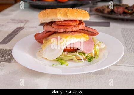 Burger mit viel Protein. Spiegelei, Schweinefleisch, Wurst, Schinken und doppelt geschmolzener Käse sowie Pepperoni auf weißem Teller Stockfoto