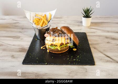 Rindfleisch-Burger mit doppeltem Fleisch, viel karamellisierte Zwiebeln mit Pilzen mit geschmolzenem Cheddar-Käse, Salat und gebratenem Speck mit einer Seite französischen Frieses Stockfoto