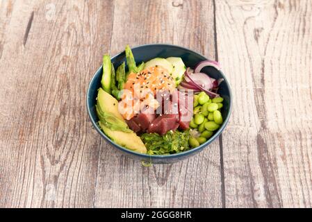 Blaue Porzellanschale gefüllt mit rotem Thunfisch, mariniertem Lachs, roter Zwiebel, grünem Wildspargel, reifen Avocados, sojasauce, Edamamabohnen, Wakame-Algen Stockfoto