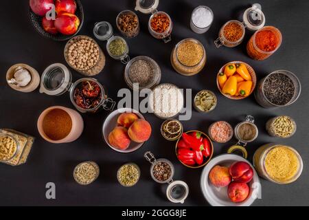 Draufsicht auf viele Glasgefäße, gefüllt mit allerlei Gewürzen und Früchten auf schwarzem Hintergrund Stockfoto