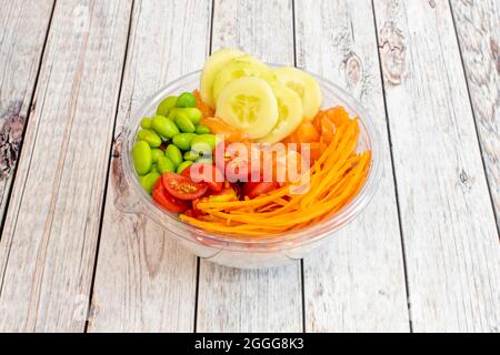 Lachsschüssel, geriebene Karotte, Kirschtomaten, edamame Bohnen, gehackte und geschälte Gurken, weißer Reis, alles in einer transparenten Lieferung nach Hause cont Stockfoto