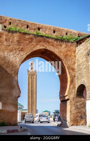 Tür in der Mauer der Medina von Rabat und im Hintergrund ein typisches marokkanisches Minarett und eine Moschee Stockfoto