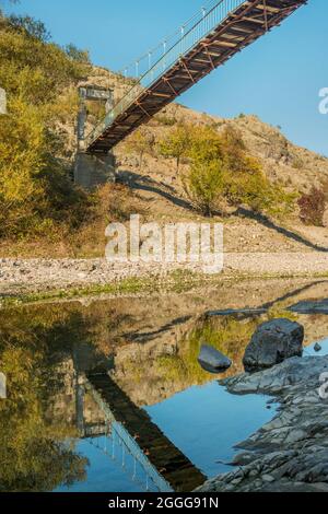 Fußgängerbrücke aus Metall und Holz und ihre Spiegelung auf der Oberfläche des Flusses Stockfoto