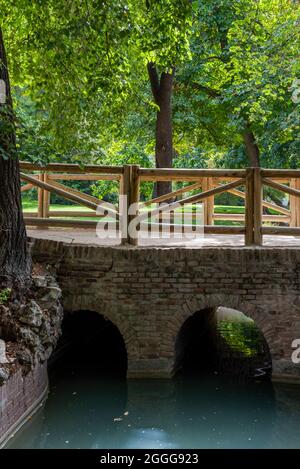 Lehmziegelbrücke mit mehreren Bögen über einem künstlichen Bach in einem Stadtpark Stockfoto