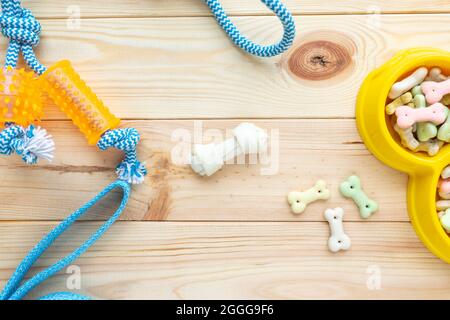 Verschiedene bunte Tierpflegezubehör: Ring, Knochen, Kugeln, Snacks auf natürlichem Holzhintergrund. Gummi- und Textilzubehör für Hunde. Stockfoto