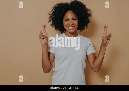 Hoffnungsvolle afroamerikanische Frau isoliert auf beigefarbenem Studiohintergrund, die Finger kreuzt und Wünsche macht Stockfoto